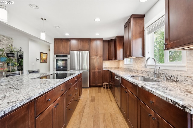 kitchen with a sink, light wood-style floors, stainless steel appliances, and light stone countertops