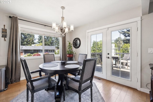 dining space featuring french doors, light wood-style floors, plenty of natural light, and an inviting chandelier