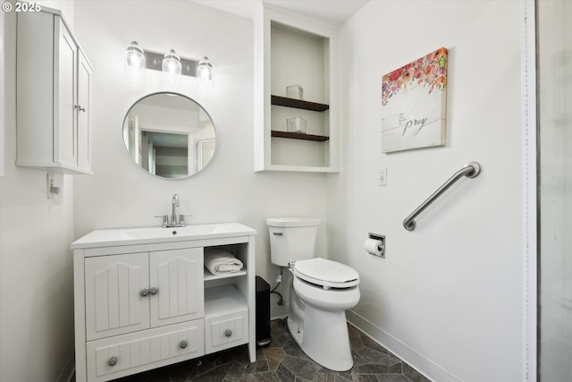 bathroom featuring toilet, baseboards, stone finish floor, and vanity