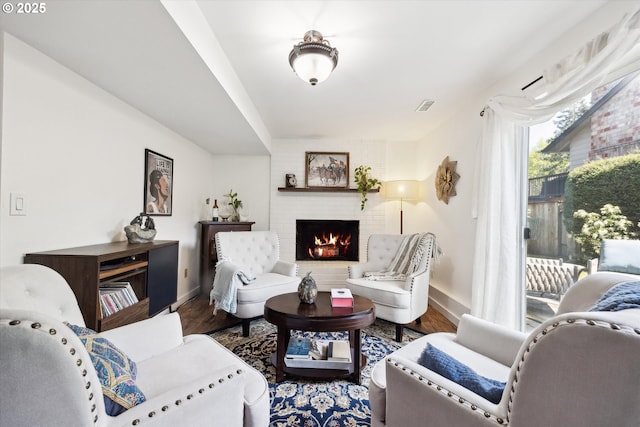 living room featuring visible vents, baseboards, a brick fireplace, and wood finished floors