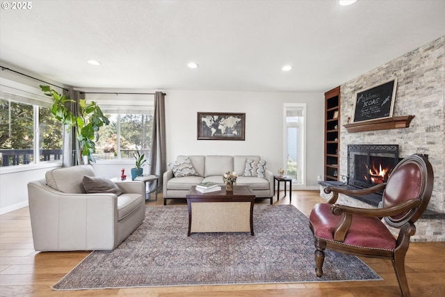 living room with a stone fireplace, recessed lighting, wood finished floors, and built in shelves