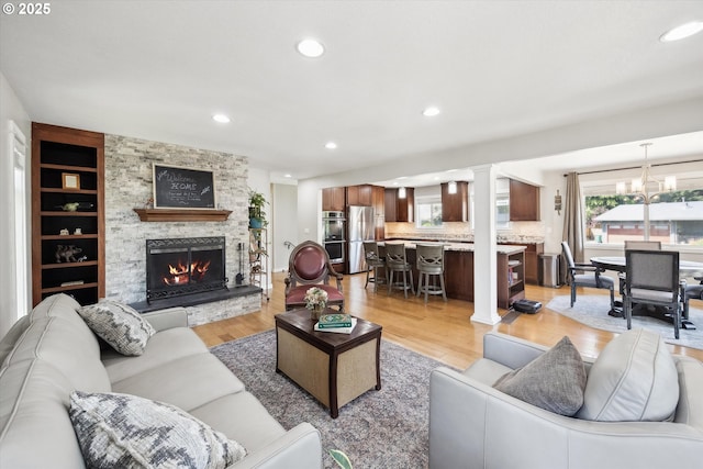 living area featuring a notable chandelier, light wood-style floors, a stone fireplace, recessed lighting, and decorative columns