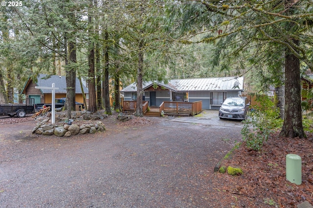 view of front facade featuring driveway, a standing seam roof, metal roof, and a wooden deck