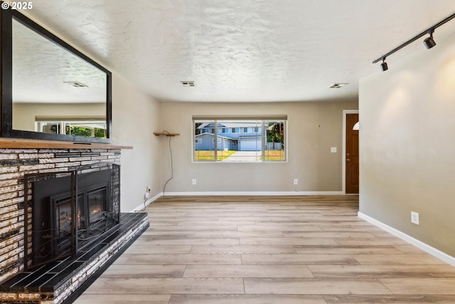 3840 Vista Dr, North Bend, OR 97459 - unfurnished living room with wood finished floors, rail lighting, a glass covered fireplace, and a textured ceiling