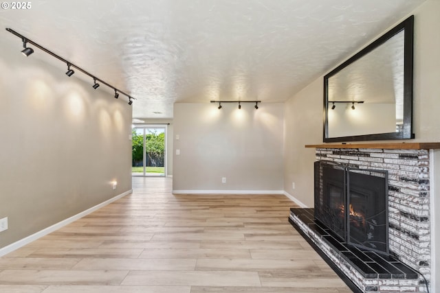 3840 Vista Dr, North Bend, OR 97459 - unfurnished living room featuring rail lighting, a glass covered fireplace, light wood finished floors, and a textured ceiling