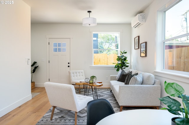 living room with baseboards, an AC wall unit, and light wood finished floors