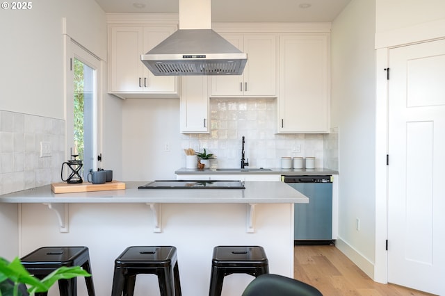 kitchen featuring black electric stovetop, wall chimney range hood, a sink, light wood-style flooring, and dishwasher