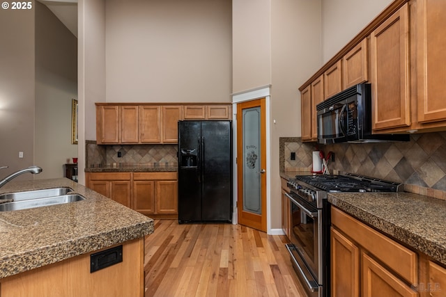 kitchen with a towering ceiling, a sink, light wood-type flooring, backsplash, and black appliances
