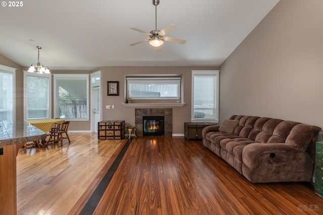 living room with ceiling fan with notable chandelier, a tile fireplace, wood finished floors, and lofted ceiling