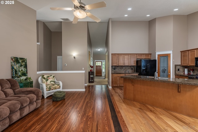 kitchen with a breakfast bar area, visible vents, a towering ceiling, black appliances, and open floor plan