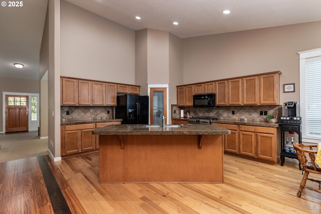 kitchen featuring brown cabinetry, a sink, high vaulted ceiling, black appliances, and light wood finished floors