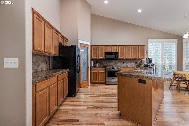 kitchen featuring decorative backsplash, a towering ceiling, a sink, black appliances, and light wood finished floors