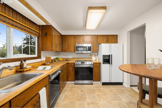 kitchen with a textured ceiling, brown cabinetry, appliances with stainless steel finishes, and a sink