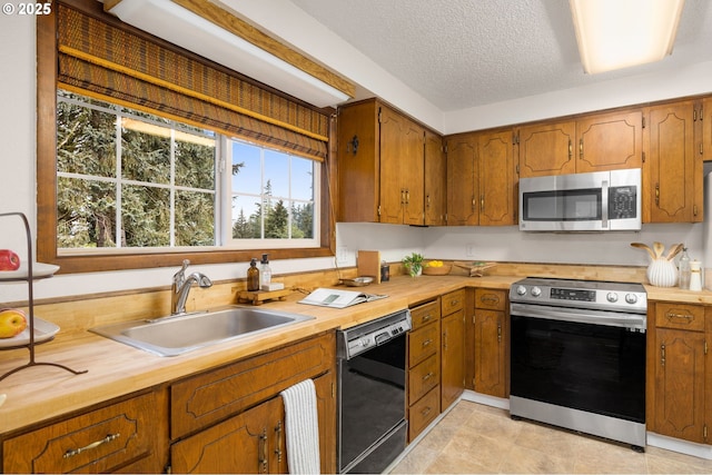 kitchen featuring wooden counters, a sink, stainless steel appliances, a textured ceiling, and brown cabinets