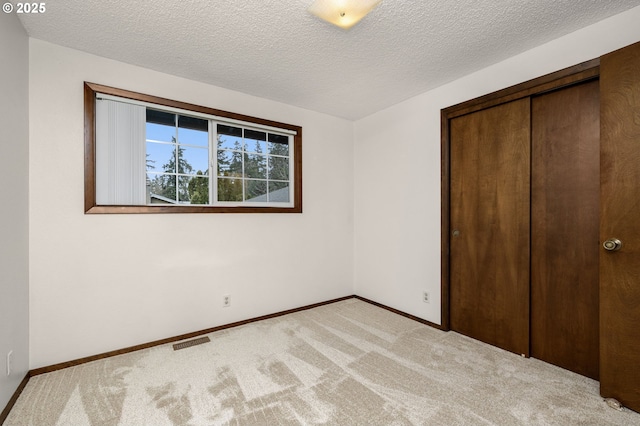 unfurnished bedroom featuring visible vents, baseboards, light carpet, a closet, and a textured ceiling