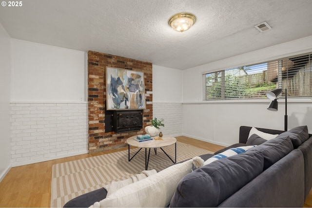 living room with visible vents, brick wall, a wainscoted wall, wood finished floors, and a textured ceiling