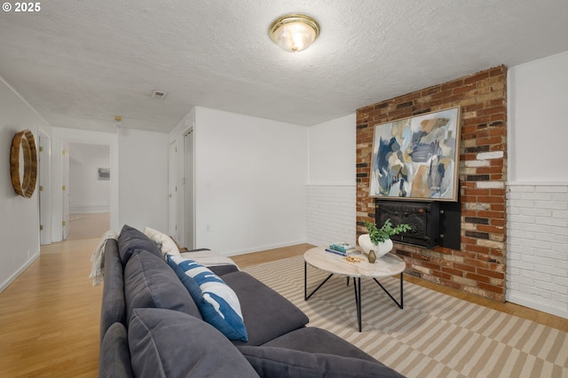 living room featuring a fireplace, wood finished floors, visible vents, and a textured ceiling