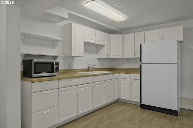 kitchen with stainless steel microwave, white cabinetry, freestanding refrigerator, and a sink