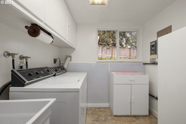 clothes washing area featuring stone finish flooring, baseboards, washer and clothes dryer, cabinet space, and a sink