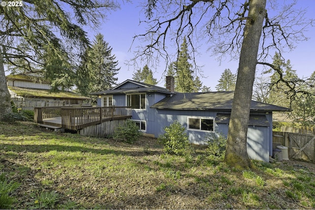 rear view of property with a chimney, a lawn, a wooden deck, and fence