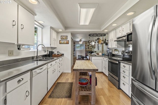 kitchen with a tray ceiling, a sink, stainless steel appliances, stainless steel countertops, and white cabinetry