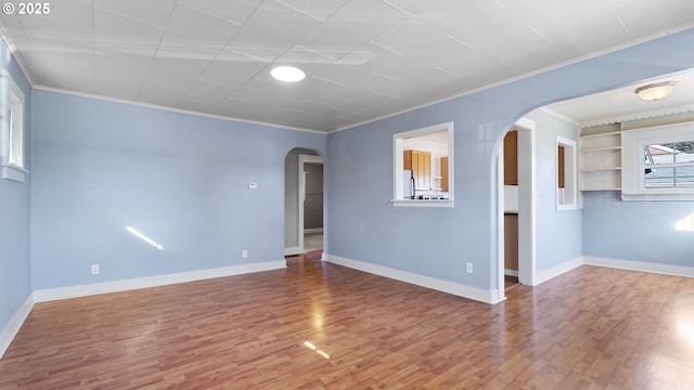 empty room with arched walkways, crown molding, wood finished floors, and baseboards