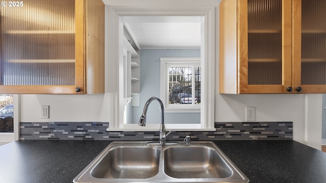 kitchen featuring backsplash, dark countertops, a sink, and glass insert cabinets