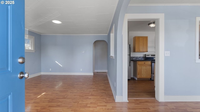 interior space featuring arched walkways, light wood finished floors, ornamental molding, and baseboards