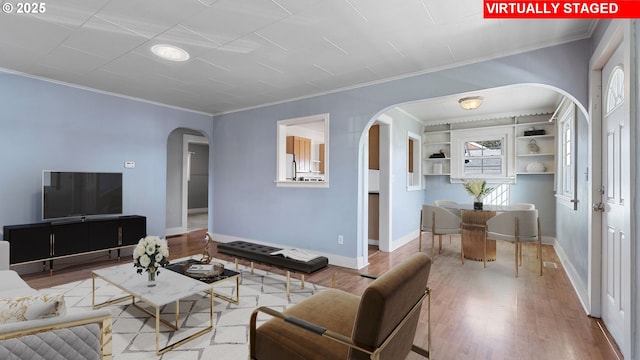 living room featuring arched walkways, ornamental molding, wood finished floors, and baseboards