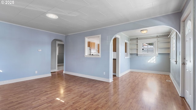 empty room featuring arched walkways, crown molding, baseboards, and wood finished floors