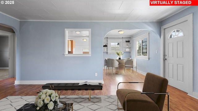 entrance foyer with arched walkways, crown molding, baseboards, and wood finished floors