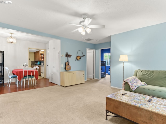 living area with visible vents, baseboards, ceiling fan with notable chandelier, and light carpet