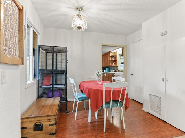 dining room with a textured ceiling, a chandelier, wood finished floors, and visible vents