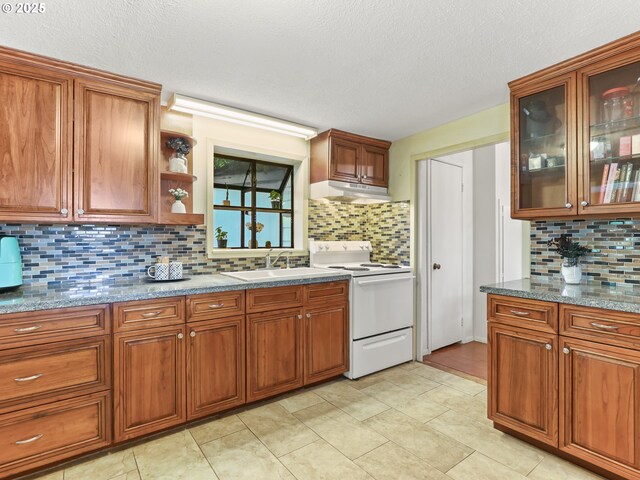 kitchen featuring brown cabinets, a sink, white range with electric cooktop, decorative backsplash, and under cabinet range hood