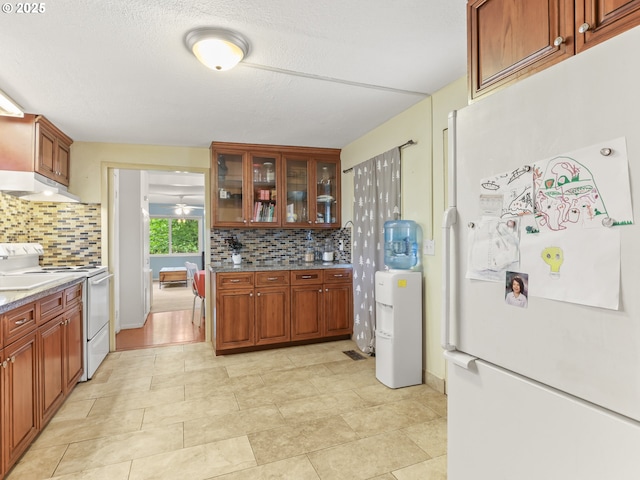 kitchen with glass insert cabinets, decorative backsplash, under cabinet range hood, and white appliances