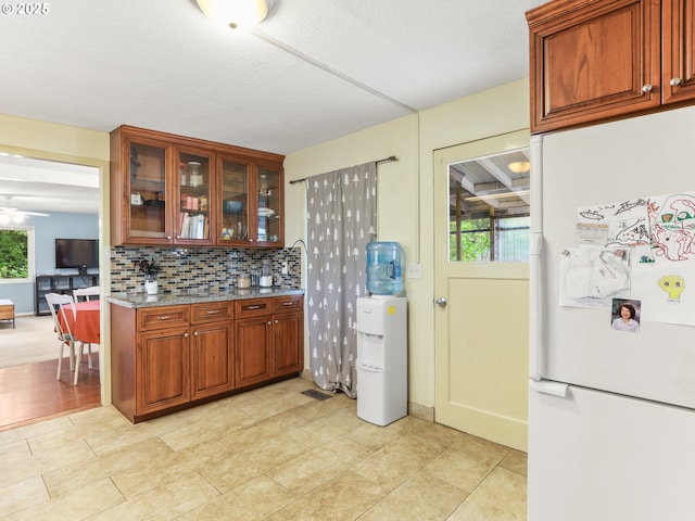 kitchen featuring freestanding refrigerator, light stone countertops, glass insert cabinets, tasteful backsplash, and light tile patterned floors