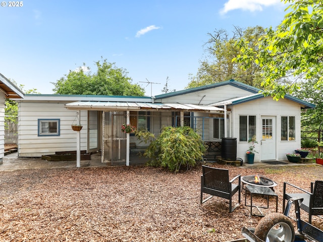 back of property with a sunroom, a fire pit, and metal roof