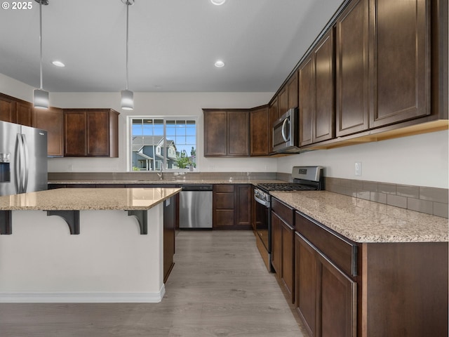 1053 Winfield St NE, Gervais, OR 97026 - kitchen with stainless steel appliances, a kitchen breakfast bar, light wood-type flooring, dark brown cabinets, and light stone countertops
