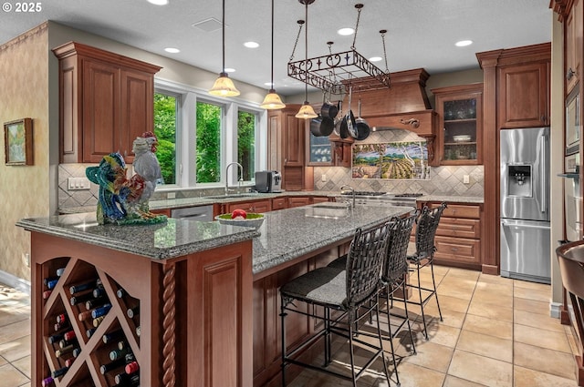 kitchen featuring appliances with stainless steel finishes, a sink, a kitchen island with sink, dark stone counters, and brown cabinets
