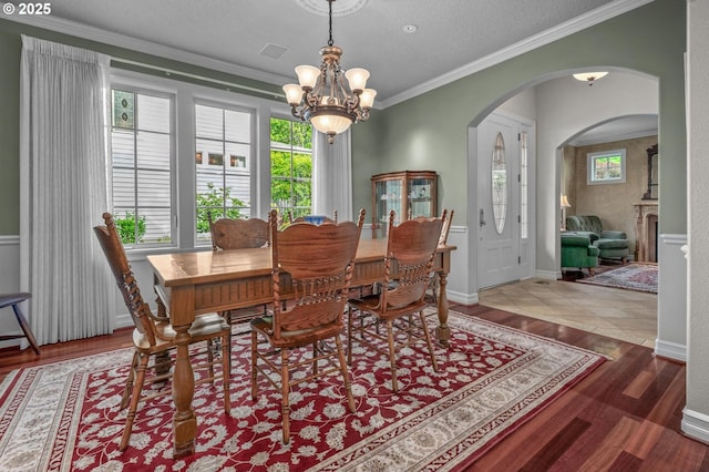 dining area featuring arched walkways, a chandelier, wood finished floors, and ornamental molding