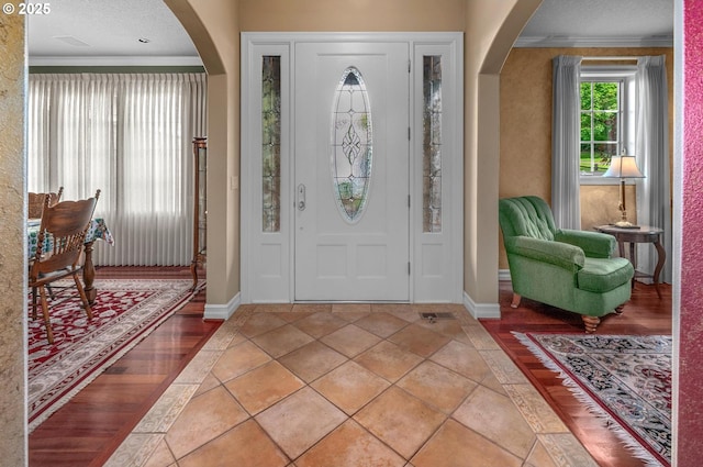 foyer entrance with arched walkways, crown molding, and baseboards