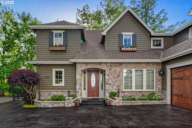 view of front of property featuring stone siding, a shingled roof, and fence