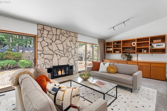 living area with a stone fireplace, vaulted ceiling, rail lighting, and visible vents