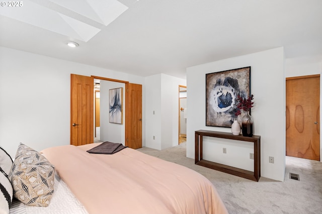 bedroom featuring light carpet, visible vents, a skylight, and ensuite bath