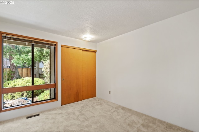 unfurnished room featuring visible vents, carpet flooring, and a textured ceiling