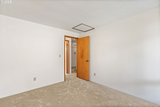 unfurnished room with a textured ceiling, attic access, and carpet floors