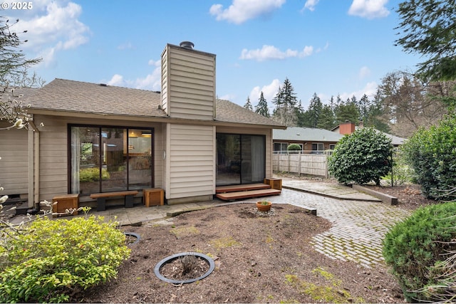 rear view of house with a chimney, a patio area, a shingled roof, and fence