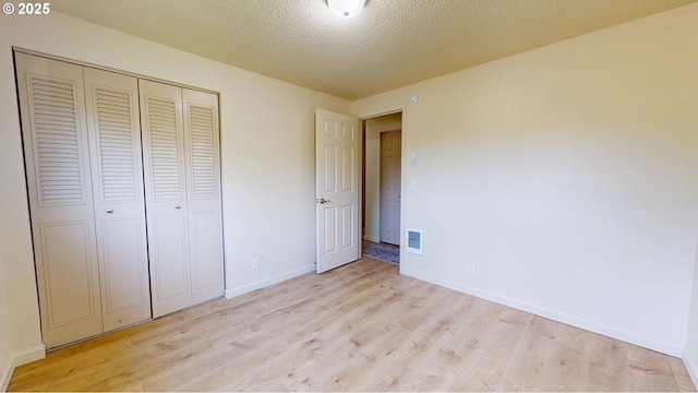 unfurnished bedroom featuring a textured ceiling, light wood-style flooring, baseboards, visible vents, and a closet