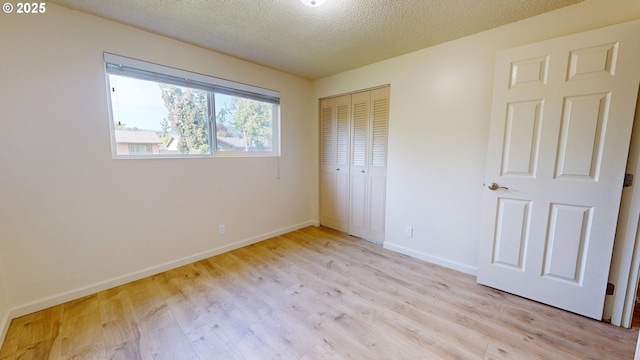 unfurnished bedroom with a closet, a textured ceiling, baseboards, and light wood-style floors