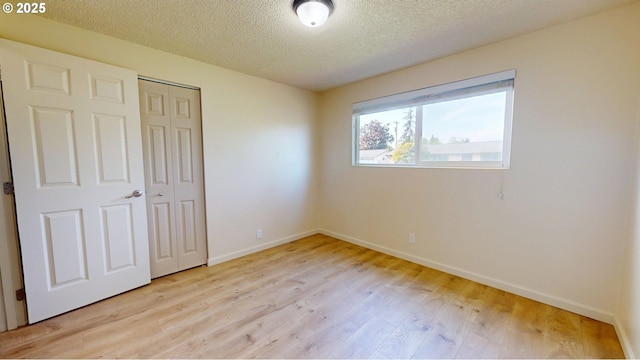 unfurnished bedroom featuring a textured ceiling, baseboards, light wood finished floors, and a closet
